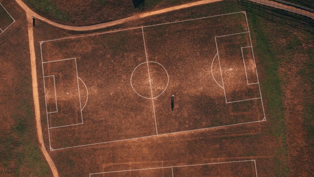 Aerial view of an empty rustic soccer field with a solitary person, showcasing detailed grass lines.